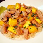 pineapple pork stir fry on a plate with rice and lime