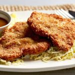 pork tonkatsu with shredded cabbages on a plate with sauce and sliced lemon